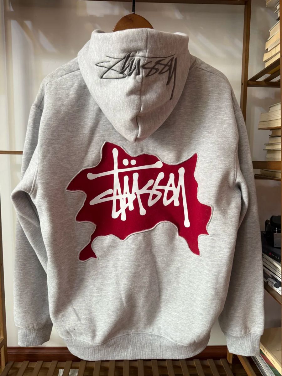 Stüssy heather grey hoodie — drawstring hood, ribbed cuffs and hem, large red and white Stüssy logo graphic on back, black Stüssy logo on hood