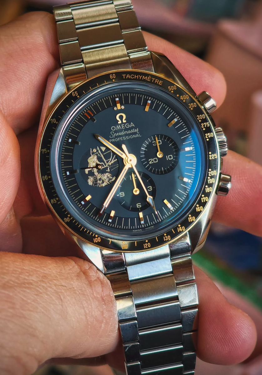 Omega dark grey and gold chronograph watch — tachymeter bezel, three subdials, gold hands and hour markers, astronaut relief on subdial, pushers on crown side, metallic bracelet