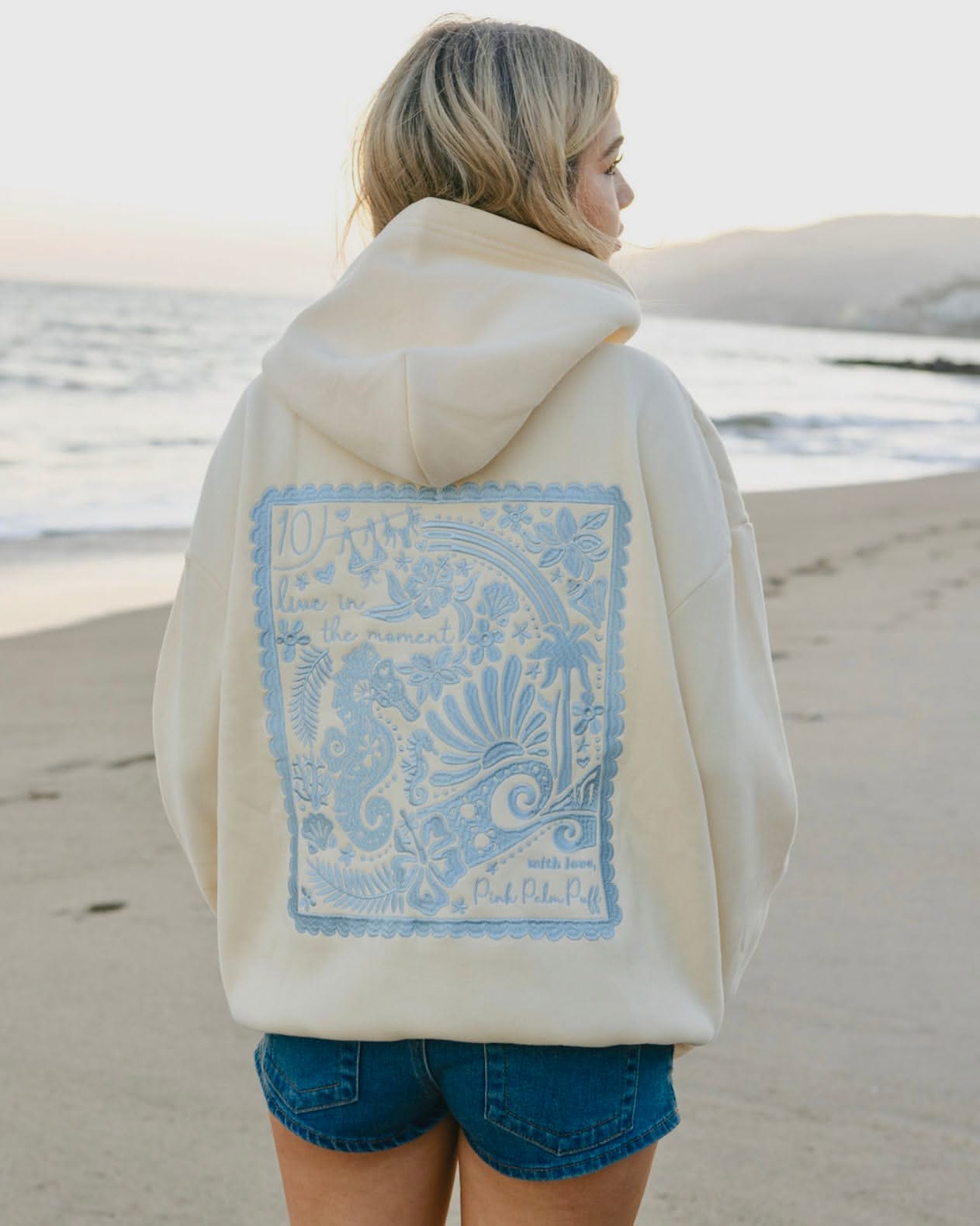 casual cream with light blue embroidery hoodie — drawstring hood, ribbed cuffs and hem, large back embroidery with marine and floral motifs, 'live in the moment' text
