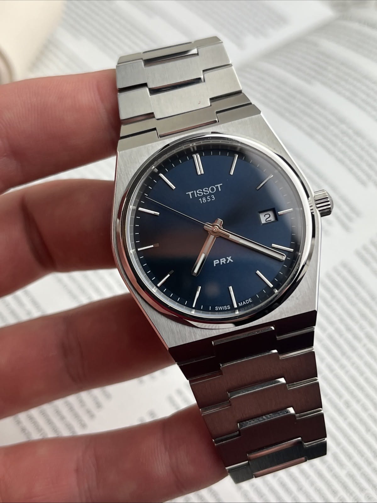 Tissot blue dial, silver-tone case watch — integrated steel bracelet, square-round case, baton hour markers, date window, brushed and polished finishes