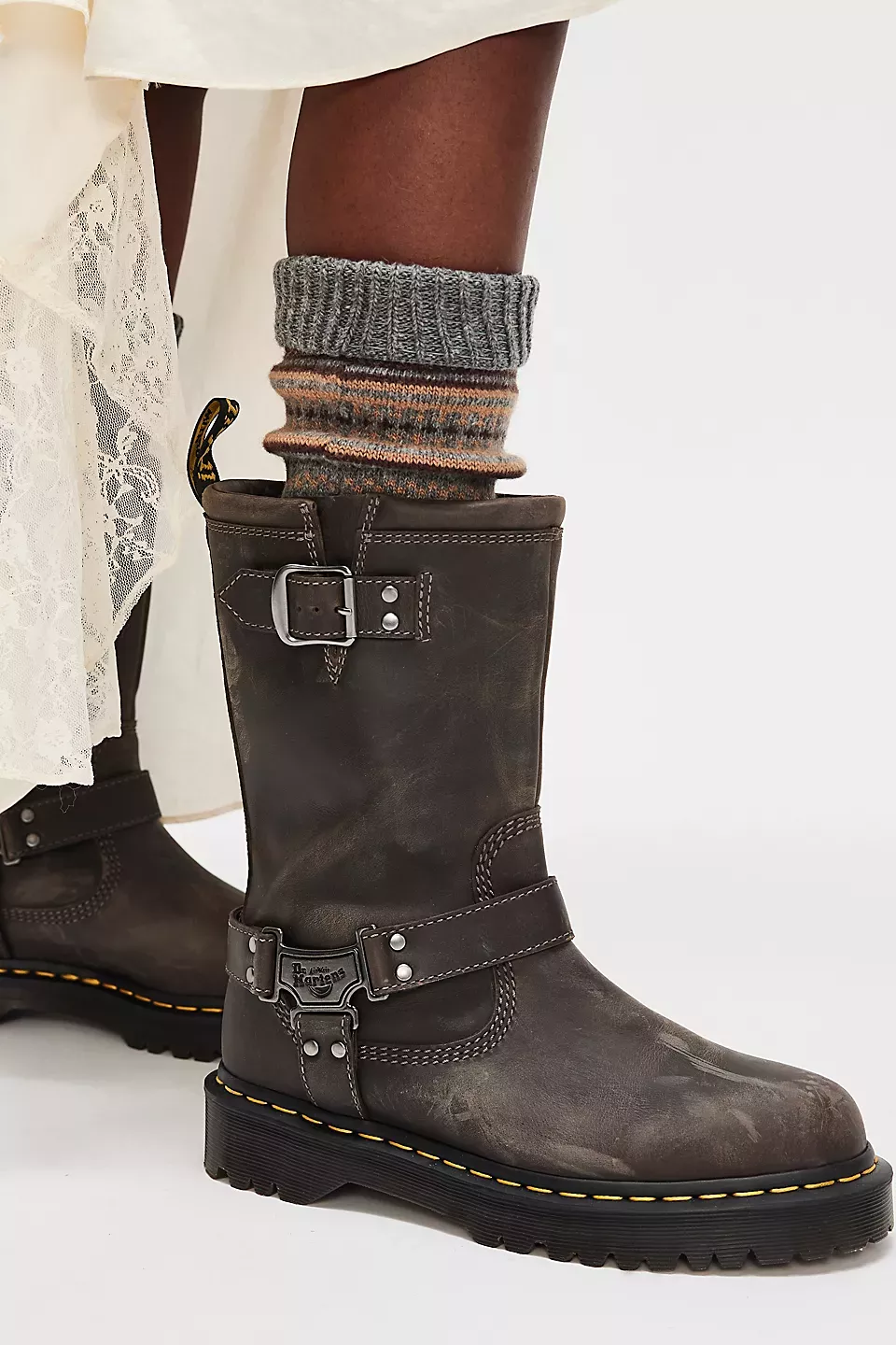 Dr. Martens distressed dark brown boots — buckle straps, harness detail, yellow welt stitching, lug sole, pull tab