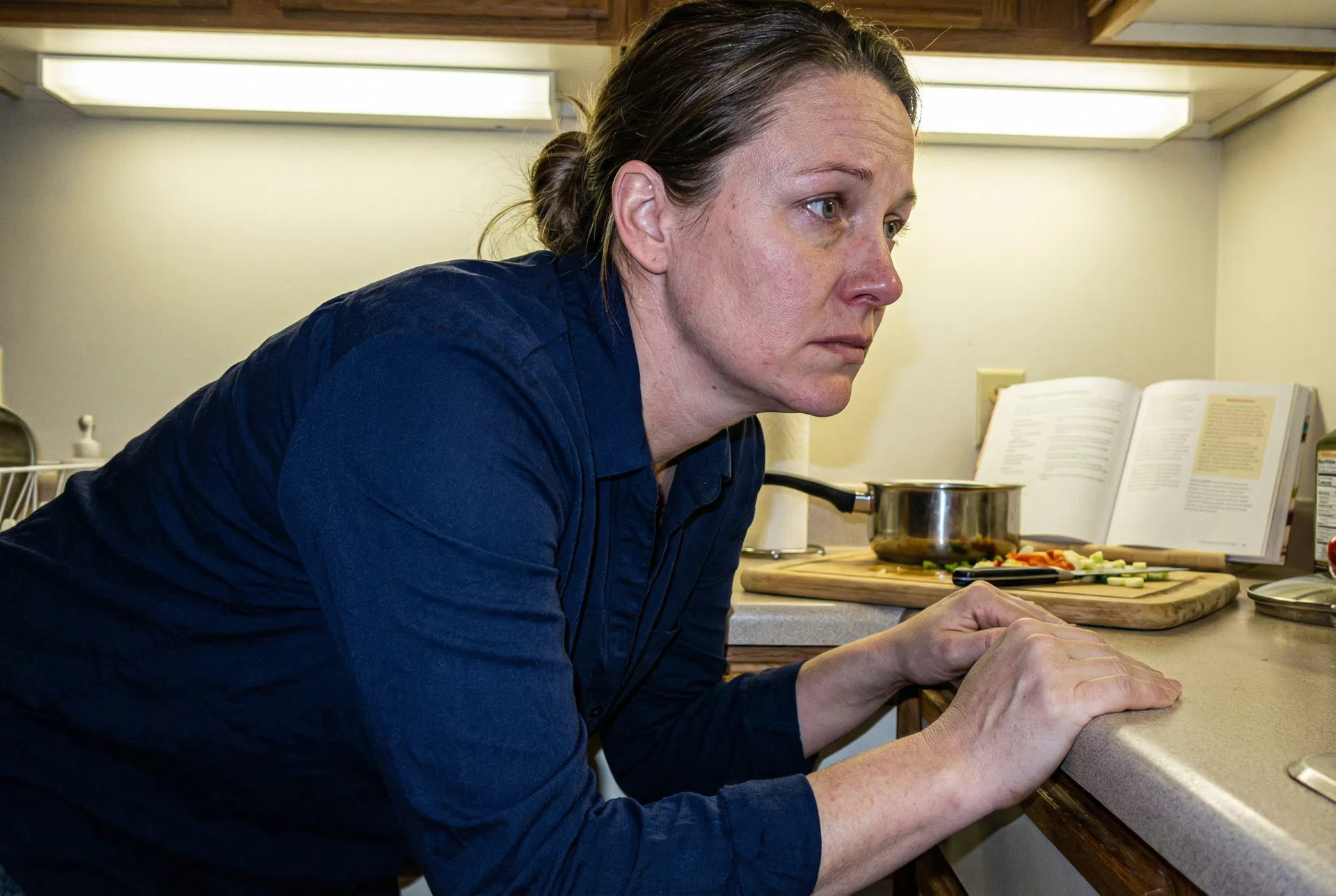Woman gripping kitchen counter, jaw clenched, holding back tears