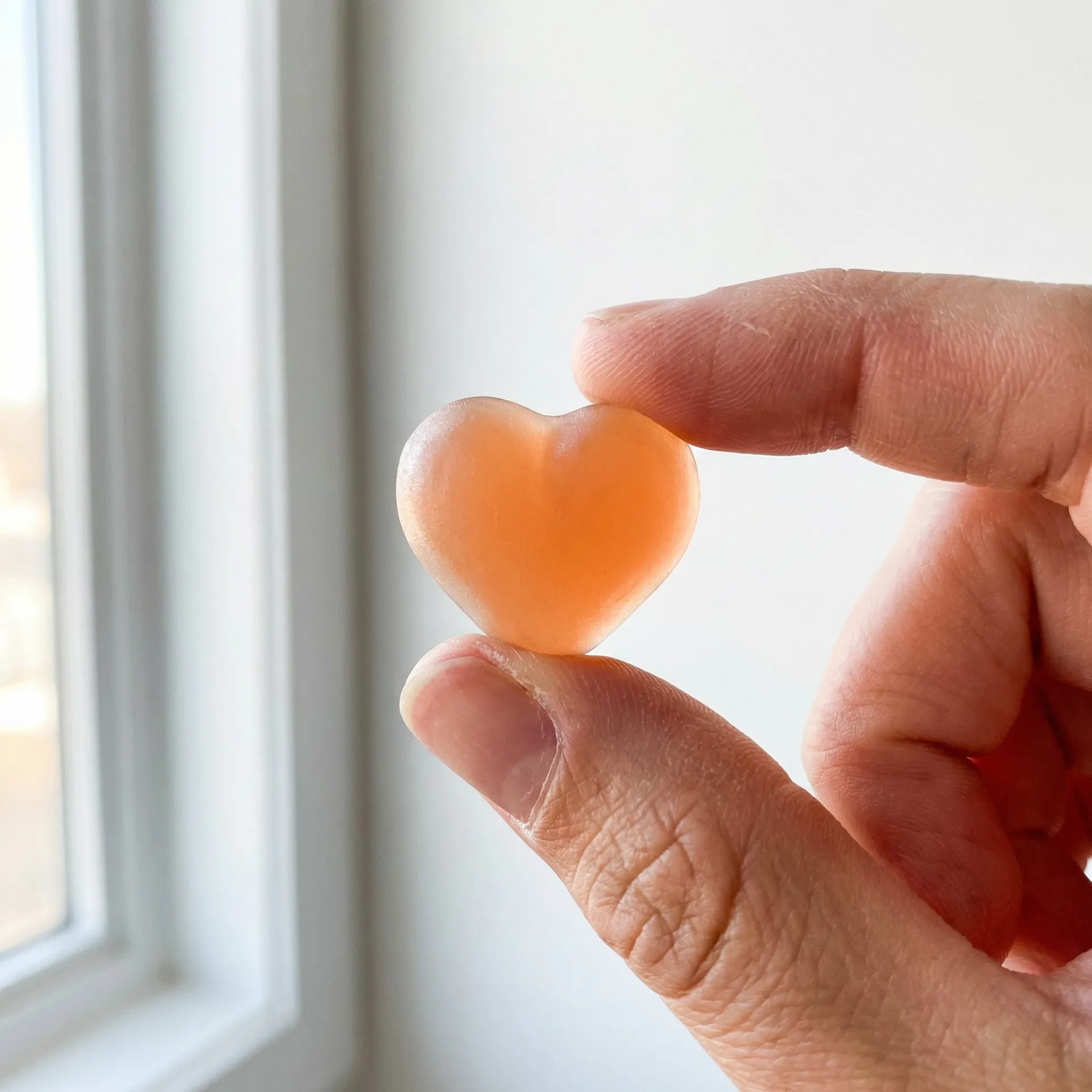 Heart-shaped peach RYVIVE gummy held between fingers in natural light