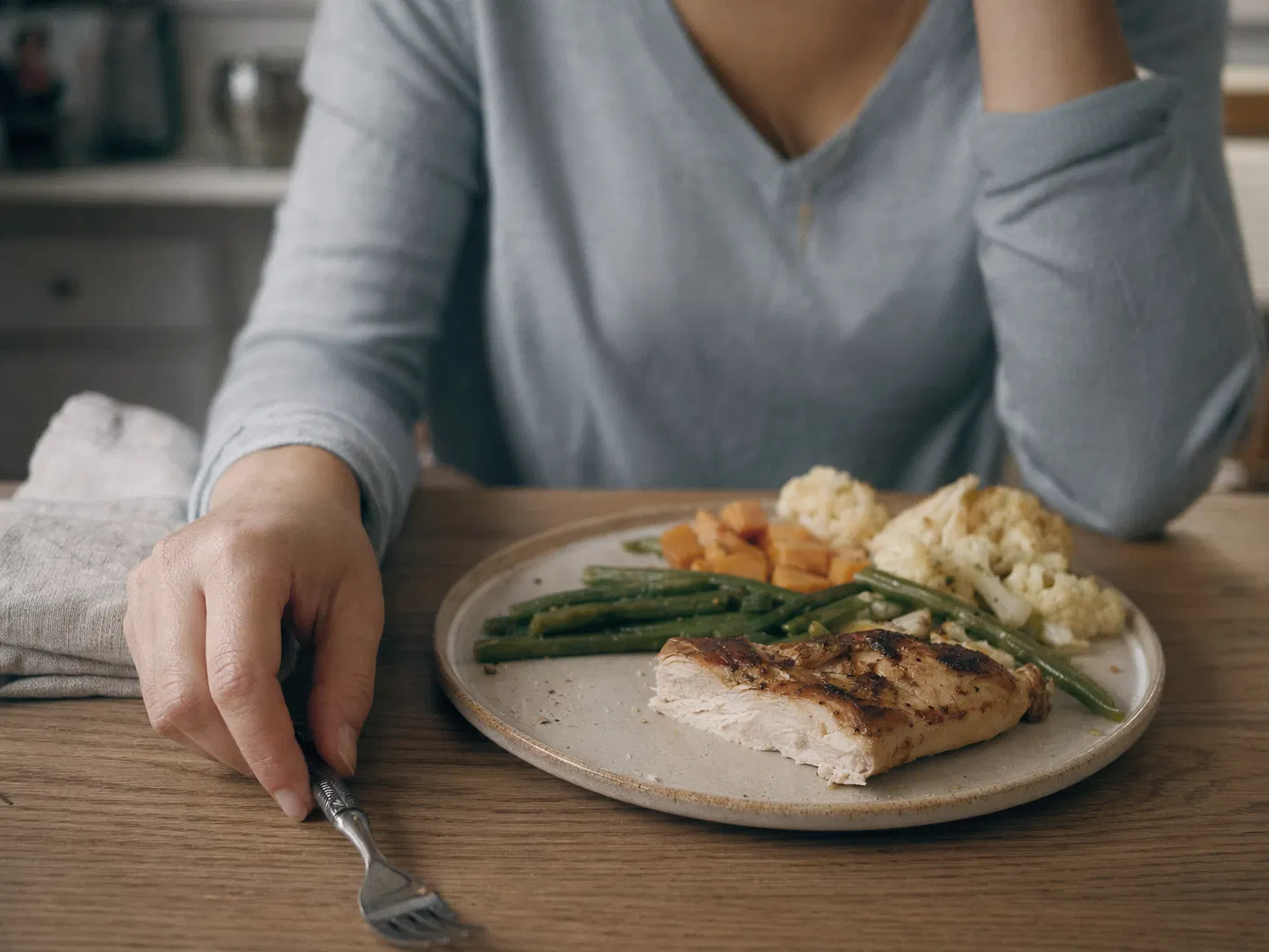 Woman at kitchen table with mostly-uneaten chicken plate, fork down — unable to eat on GLP-1