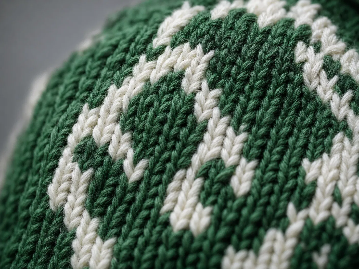 Extreme macro close-up of jacquard knit texture showing interlocking green and cream yarn stitches