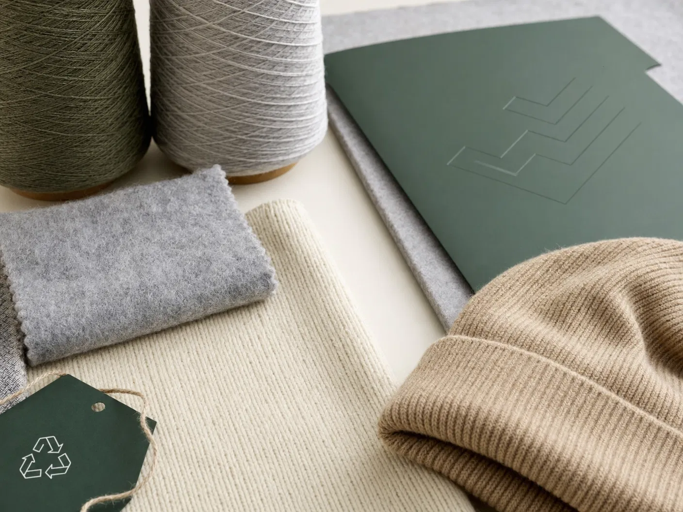 Premium material and compliance support still life with recycled yarn cones, knit swatches, blank document folder and thermal beanie edge