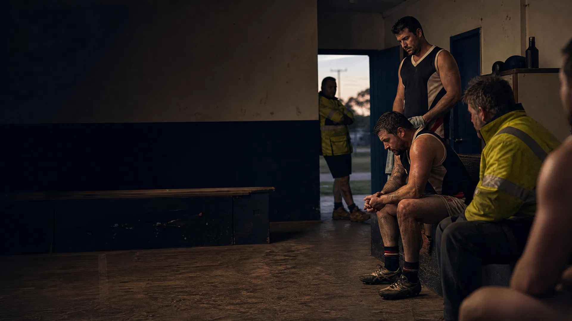 A grounded footy changeroom moment with Australian working men in quiet conversation