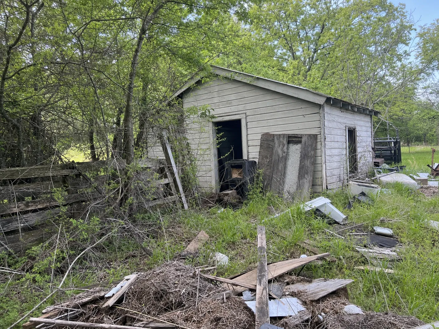 Before demolition showing an old small building with brush and debris around the property edge
