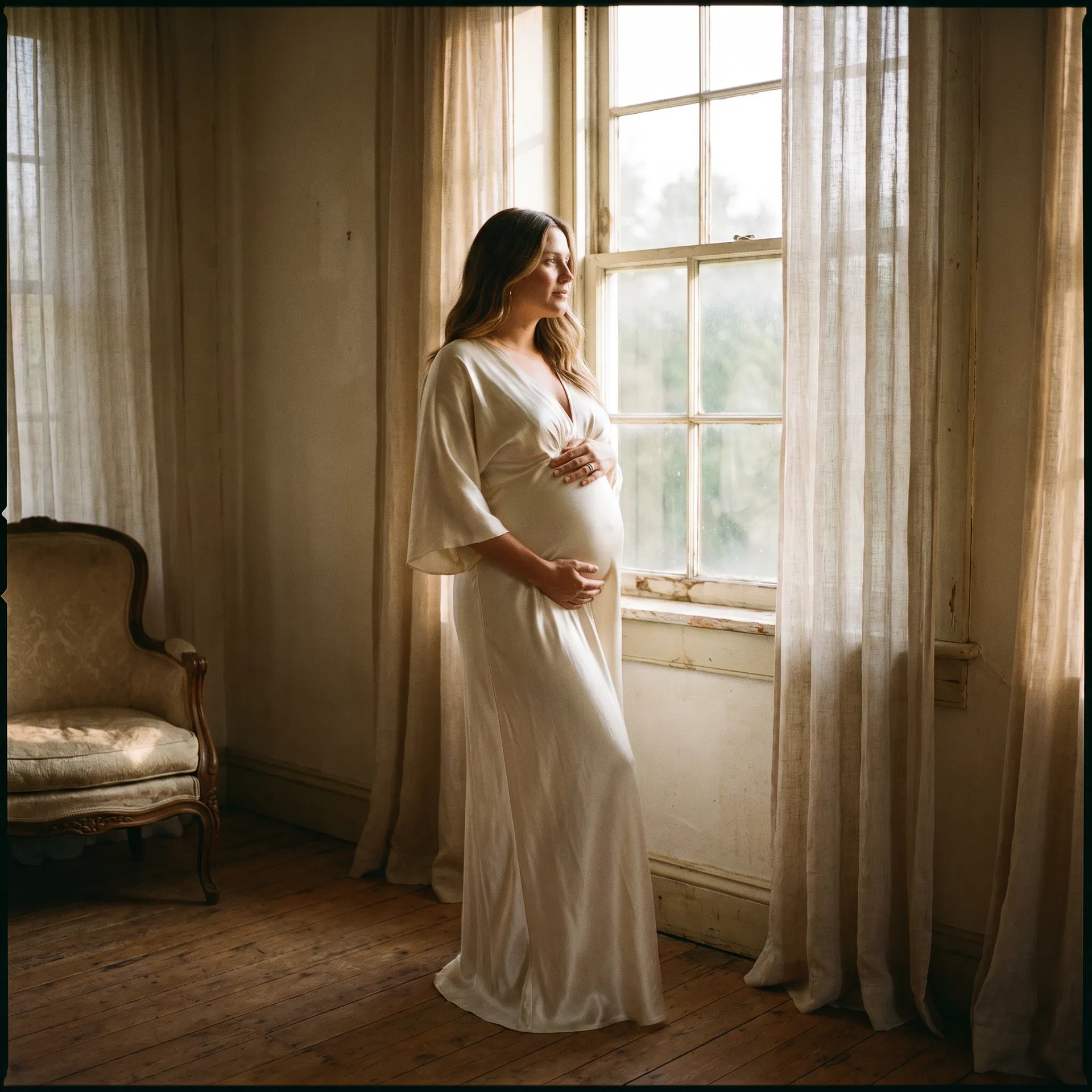 Maternity portrait by window in ivory dress
