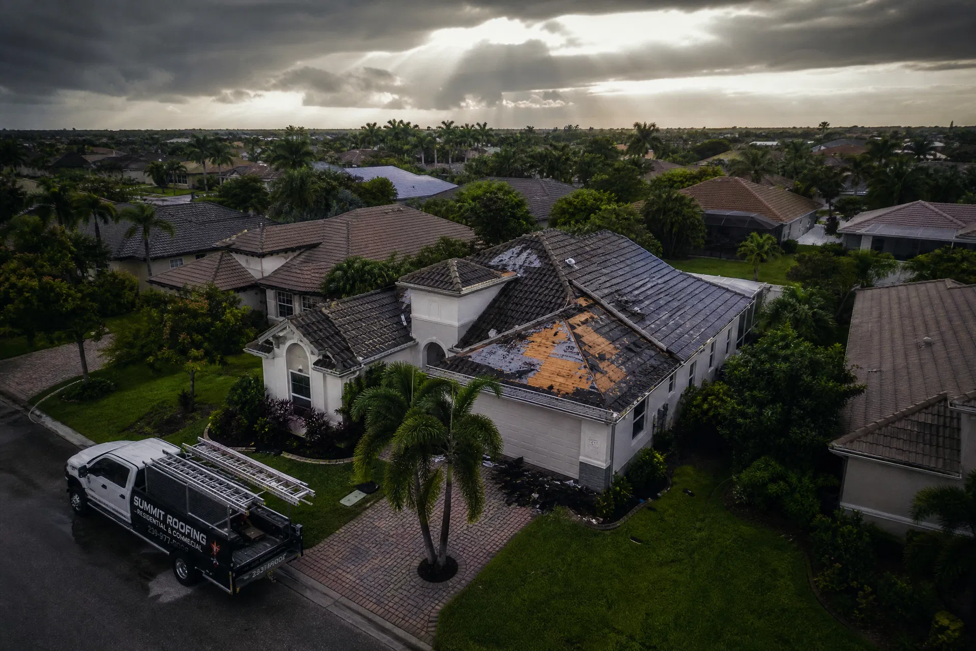 Aerial view of Florida rooftops after a storm with a roofing contractor truck parked outside a damaged home