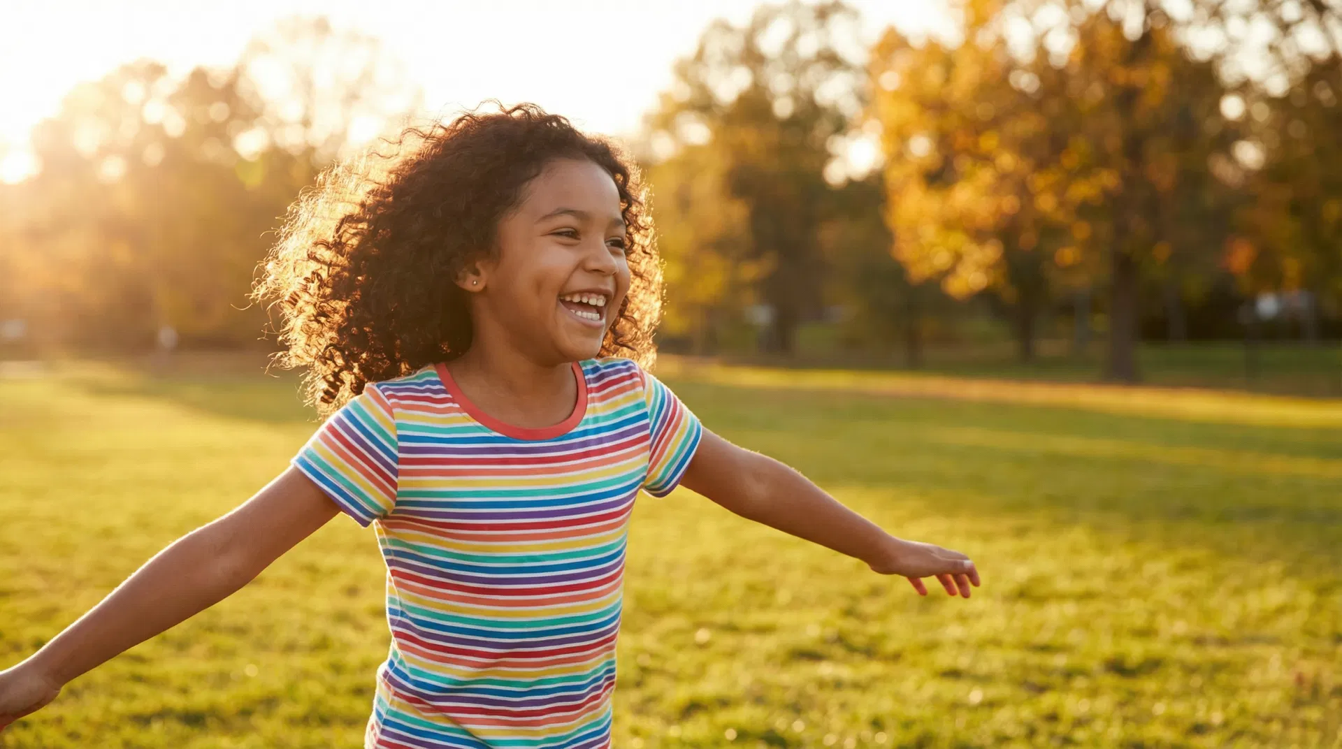 A joyful Hispanic girl running and playing outside in a sunny park with arms wide open, no glasses