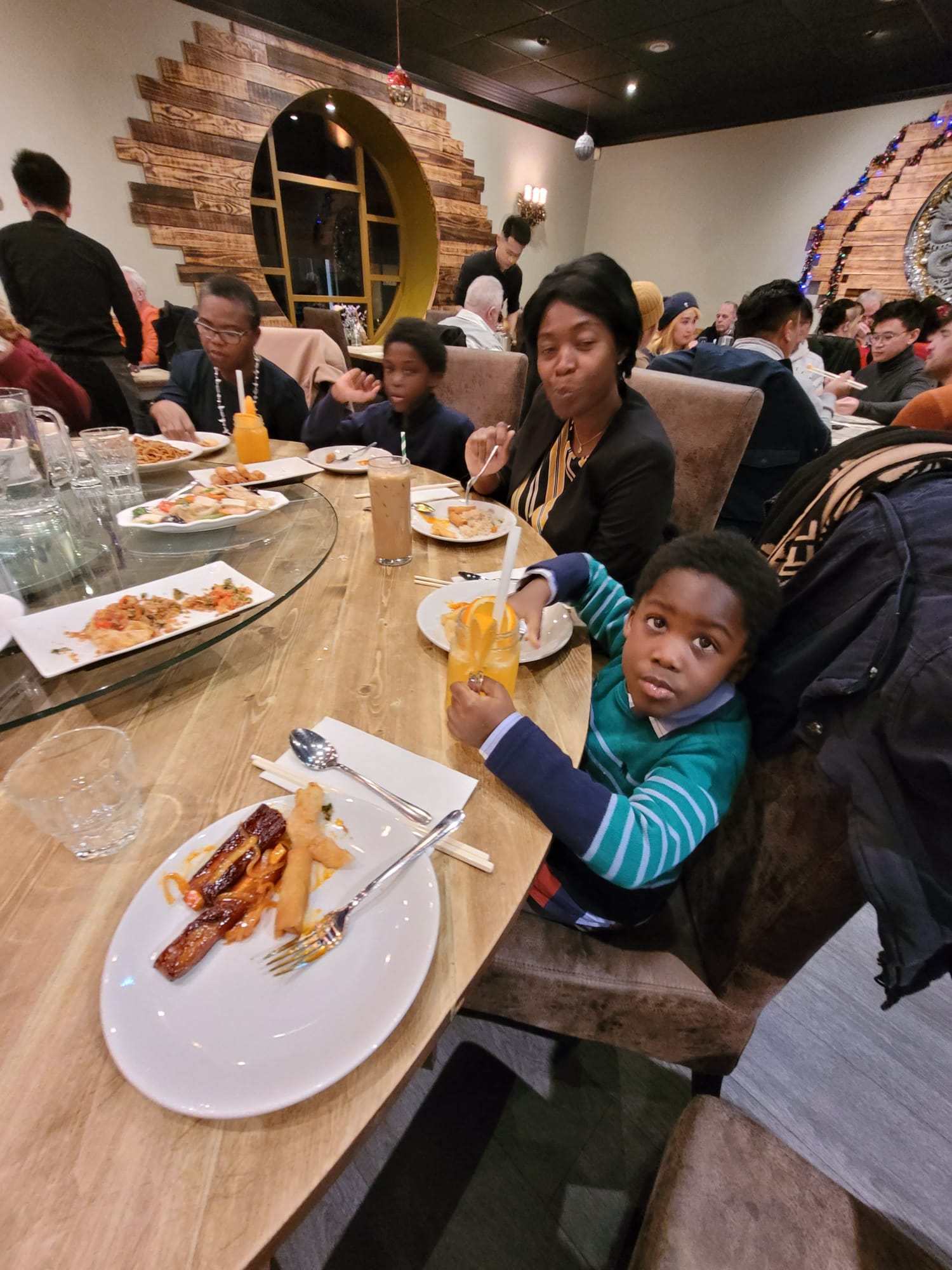 Young boy with orange juice and woman dining in a busy Christmas-decorated restaurant