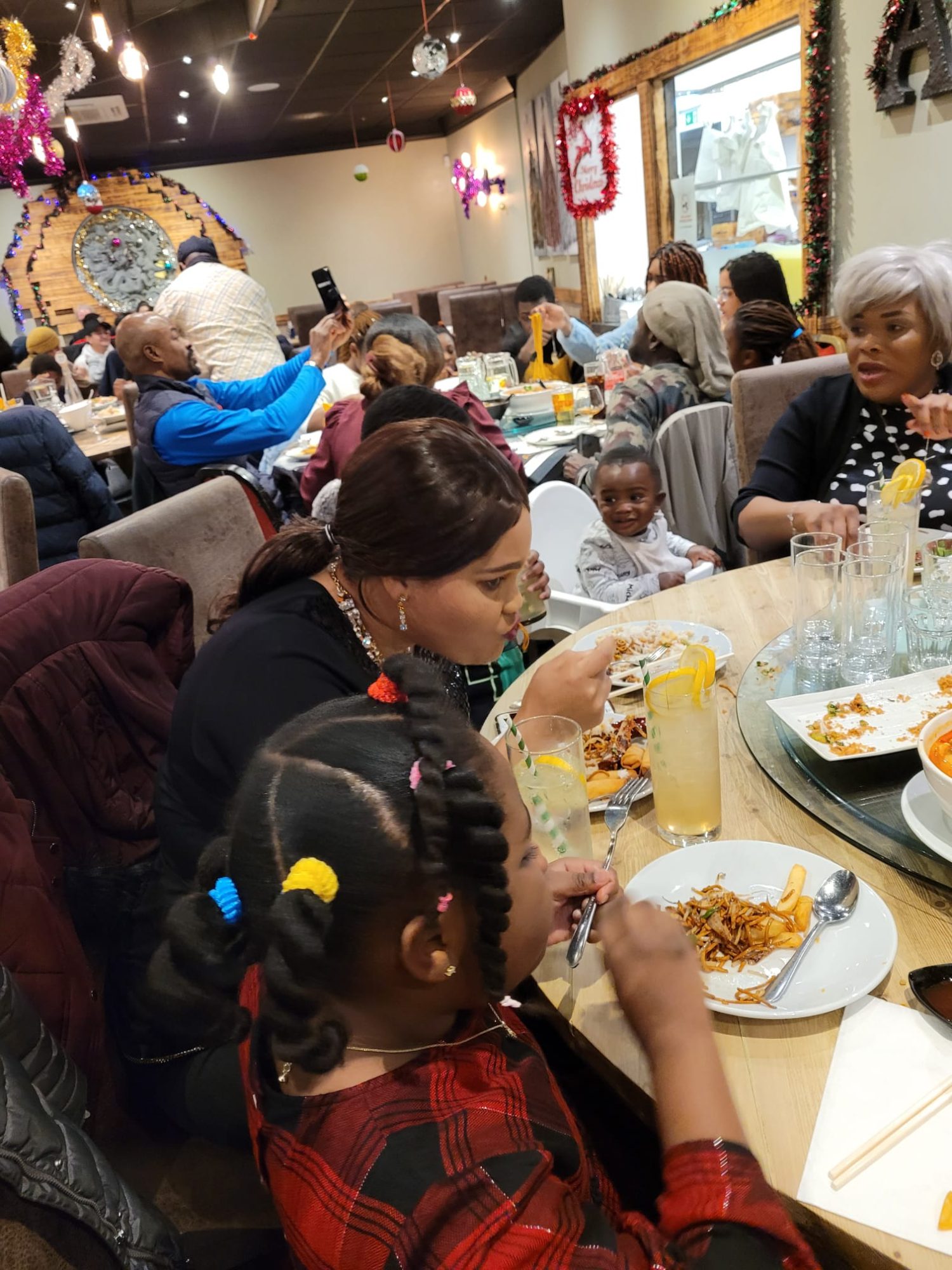 Girl and women dining with a smiling toddler in a restaurant filled with Christmas decorations